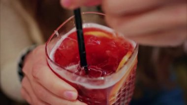 Kırmızı kokteyli siyah pipetle karıştıran bir kadının yakın çekimi.