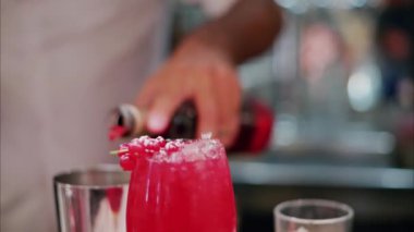 Close up of a red cocktail with a blurry view of a barman preparing a drink in the background