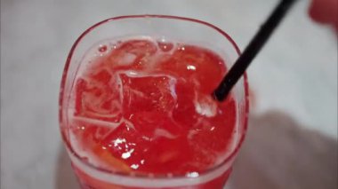 Kırmızı kokteyli siyah pipetle karıştıran bir kadının yakın çekimi.