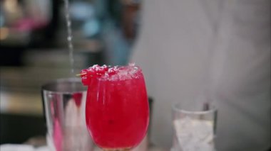 Arka planda içki hazırlayan barmenin bulanık manzaralı kırmızı bir kokteyli kapat.