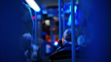 İnsanlar akşam hareket halindeki bir trende mavi ışıkla oturuyorlar.