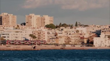 Kıyıdaki binaların ve palmiye ağaçlarının önünde hareket eden tren arka planda Fransa 'nın Antibes kentindeki dağları görüyor.