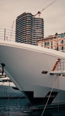 Monaco Marina 'ya yanaşmış arka planda binalar olan teknelerin yakın görüntüsü. Dikey