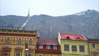 The facade of multiple, old style buildings in Brasov, Romania with a view of the mountains on the background