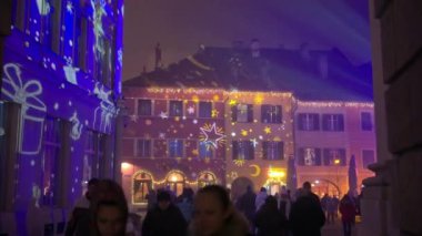 Brasov, Romanya - 20 Aralık 2024: İnsanlar şehir merkezinde arka plandaki binalarla ilgili Noel projeksiyonlarıyla yürüyorlar