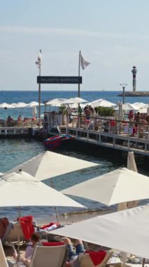 Cannes, Fransa - 15 Ekim 2024: İnsanlar sahilde şemsiye altında dinleniyor. Dikey