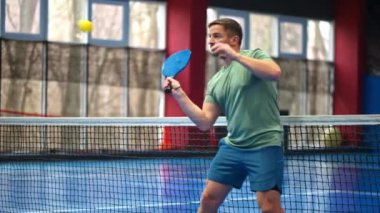 Yeşil tişörtlü bir adam mavi, iç sahada penisbol oynuyor.