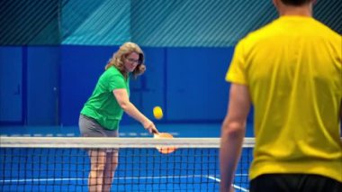 Bir adam ve bir kadın, mavi bir sahada, bir penisbol oynuyor.