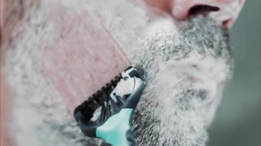 Sakalını jiletle tıraş eden bir adamın yakın çekimi.