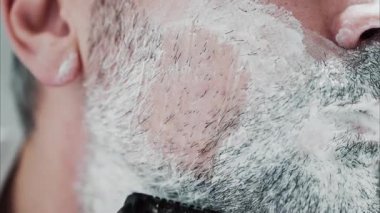 Sakalını jiletle tıraş eden bir adamın yakın çekimi.