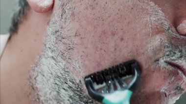 Sakalını jiletle tıraş eden bir adamın yakın çekimi.