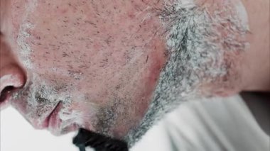 Sakalını jiletle tıraş eden bir adamın yakın çekimi.