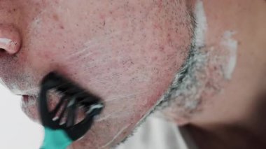Sakalını jiletle tıraş eden bir adamın yakın çekimi.