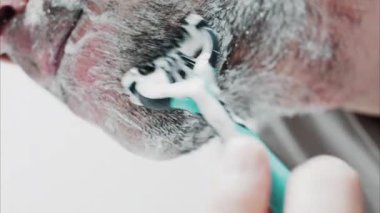 Sakalını jiletle tıraş eden bir adamın yakın çekimi.