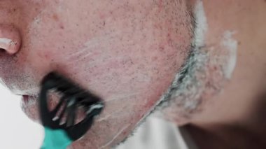 Sakalını jiletle tıraş eden bir adamın yakın çekimi.