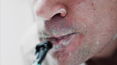 Sakalını jiletle tıraş eden bir adamın yakın çekimi.