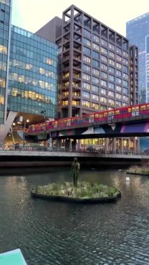 Londra, İngiltere - 27 Kasım 2024: Kanarya Rıhtımı 'nda raylarda ilerleyen kırmızı tren ve akşam saatlerinde arka planda binalar. Dikey