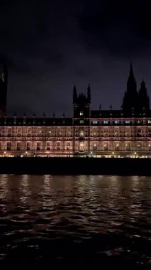 İngiltere 'nin başkenti Londra' da akşam vakti Thames Nehri 'nin yanındaki Westminster Sarayı' nın hareket halindeki bir teknesinden görüntü. Dikey