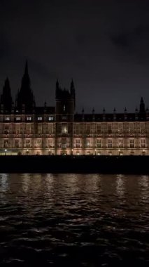 İngiltere 'nin başkenti Londra' da akşam vakti Thames Nehri 'nin yanındaki Westminster Sarayı' nın hareket halindeki bir teknesinden görüntü. Dikey