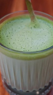 Bir kafe 'de matcha lattesini kağıt kamışla karıştıran bir kadının yakın çekimi. Dikey