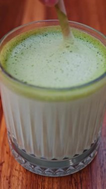 Bir kafe 'de matcha lattesini kağıt kamışla karıştıran bir kadının yakın çekimi. Dikey
