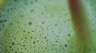 Bir kafe 'de kamışla kibrit latteyi karıştıran bir kadının yakın plan fotoğrafı.