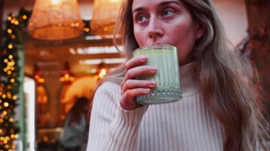 Bir kafede kağıt kamışla matcha latte içen bir kadının yakın çekimi.