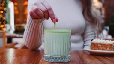 Bir kafe 'de kamışla kibrit latteyi karıştıran bir kadının yakın plan fotoğrafı.