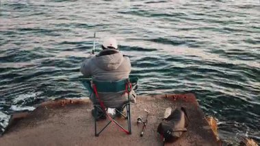 Kışlık elbiseli bir adam Fransa 'nın güneyinde denizde balık tutan bir sandalyede.