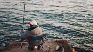 Kışlık elbiseli bir adam Fransa 'nın güneyinde denizde balık tutan bir sandalyede.