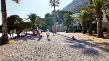 Beaulieu-sur-Mer, Fransa - 5 Temmuz 2024: İnsanlar sahilde yürüyor ve Petite Afrique Sahili 'nde dinleniyorlar