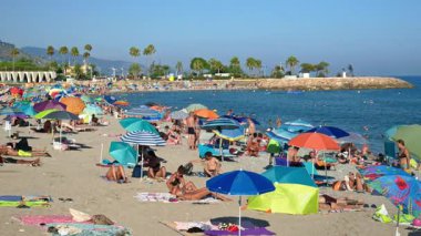 Menton, Fransa - 4 Eylül 2024: İnsanlar güneşli şemsiyeler altında sahilde yüzüyor ve dinleniyorlar