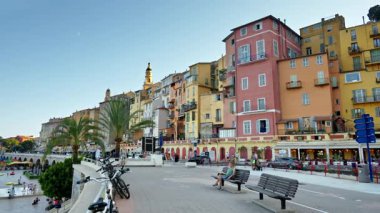 Menton, Fransa - 4 Eylül 2024: Şehirdeki renkli binaların ve kıyı şeridinde yürüyen insanların görüntüsü