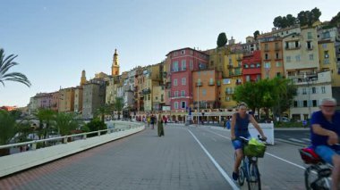 Menton, Fransa - 4 Eylül 2024: Şehirdeki renkli binaların ve kıyı şeridinde yürüyen insanların görüntüsü