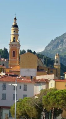Menton, Fransa - 4 Eylül 2024: St. Michel Bazilikası 'nın renkli binalarla çevrili uzak manzarası. Dikey