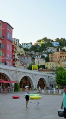 Menton, Fransa - 4 Eylül 2024: Şehirdeki renkli binaların ve kıyı şeridinde yürüyen insanların görüntüsü. Dikey