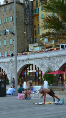 Menton, Fransa - 4 Eylül 2024: Şehirdeki renkli binaların ve kıyı şeridinde yürüyen insanların görüntüsü. Dikey