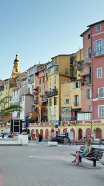 Menton, Fransa - 4 Eylül 2024: Şehirdeki renkli binaların ve kıyı şeridinde yürüyen insanların görüntüsü. Dikey