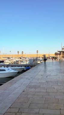 Menton, Fransa - 4 Eylül 2024: Fransız Rivierası 'ndaki Port de Menton limanında teknelerin yanında yürüyen insanlar. Dikey