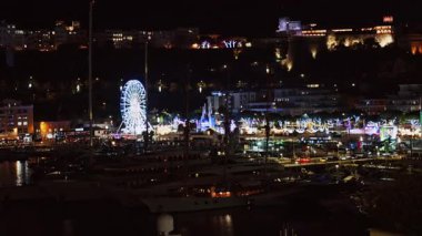 Monako 'daki Hercule Funfair Limanı' ndaki aydınlık dönme dolabın uzaktan görüntüsü.