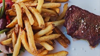 Restoranda beyaz bir tabakta patates kızartması ve salatayla kazığı yakın.