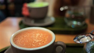 Arka planda matcha latte içen bir kadının bulanık görüntüsü olan bir kafedeki masanın üzerindeki kapuçinoyu kapat.