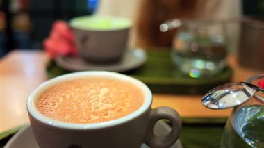 Arka planda matcha latte içen bir kadının bulanık görüntüsü olan bir kafedeki masanın üzerindeki kapuçinoyu kapat.