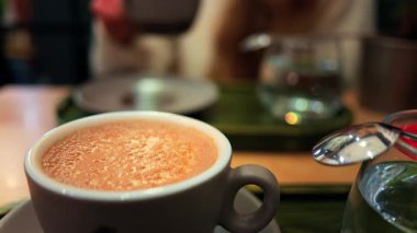 Arka planda matcha latte içen bir kadının bulanık görüntüsü olan bir kafedeki masanın üzerindeki kapuçinoyu kapat.