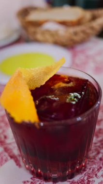 Lokantadaki kırmızı beyaz masa örtüsüne negroni kokteyli koy. Dikey