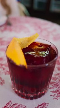 Lokantadaki kırmızı beyaz masa örtüsüne negroni kokteyli koy. Dikey