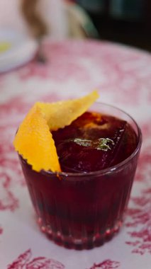 Lokantadaki kırmızı beyaz masa örtüsüne negroni kokteyli koy. Dikey