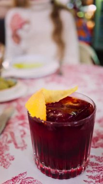 Arka planda bir restoranda içki içen bir kadınla kırmızı ve beyaz masa örtüsünün üzerinde negroni kokteyli yakın plan. Dikey