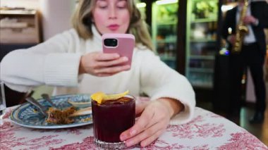Restoranda kırmızı ve beyaz masa örtüsü üzerinde negroni kokteyli çeken bir kadının fotoğrafını çek.