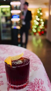 Arka planda bir restoranda içki içen bir kadınla kırmızı ve beyaz masa örtüsünün üzerinde negroni kokteyli yakın plan. Dikey